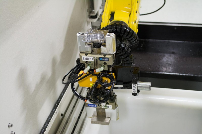 This robotic arm is in the process of reorienting the trigger component on the top while preparing a new block of metal for milling on the bottom.
