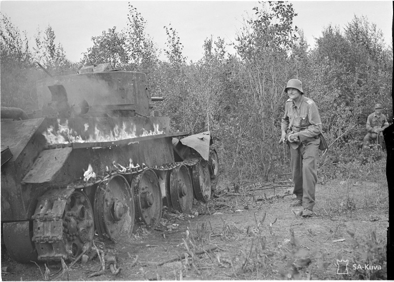 A Finnish soldier walks past a burning Soviet tank. The tank appears to be a BT-7. Date taken: August 5, 1941.